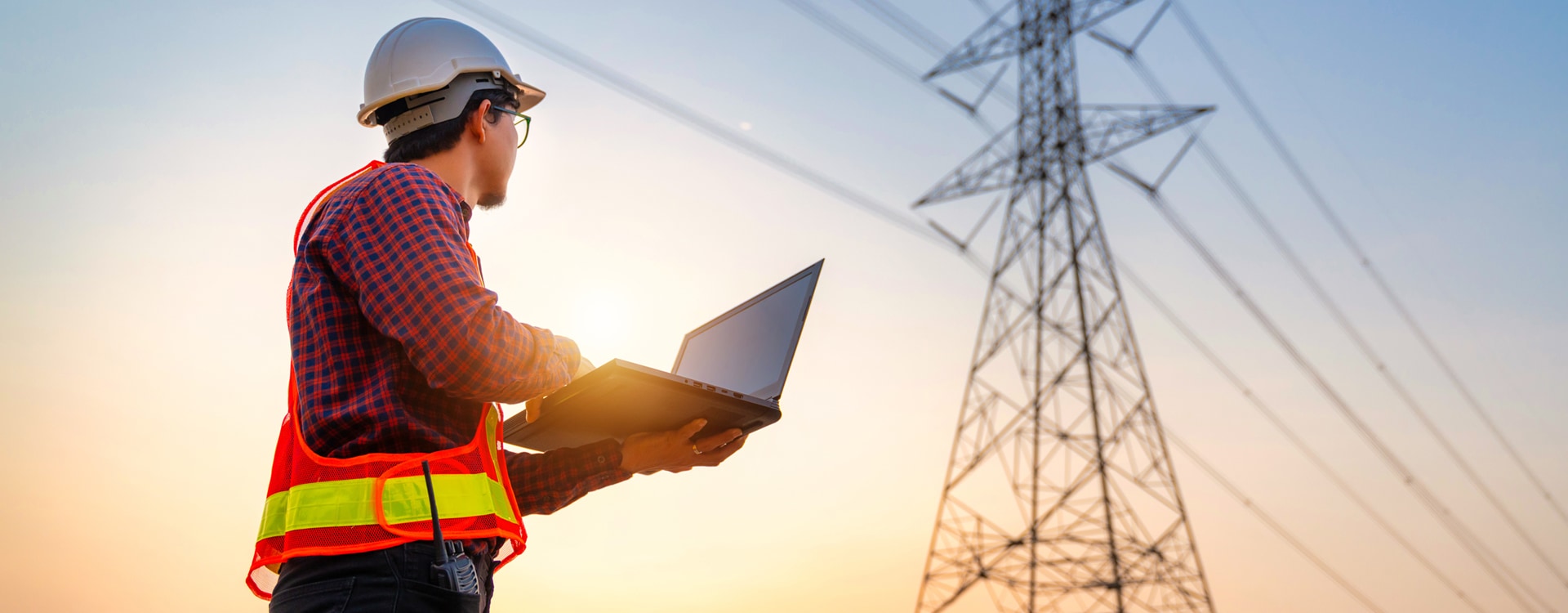 Techniker mit Laptop in der Hand vor einem Strommast